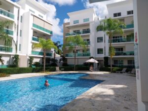 Renditestarke Immobilien Punta Cana mit Pool im Innenhof. Die Balkone haben eine türkise Glasumrandung.