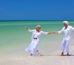 Ein Paar ältere hübsche menschen tanzen am Strand ganz in weiß